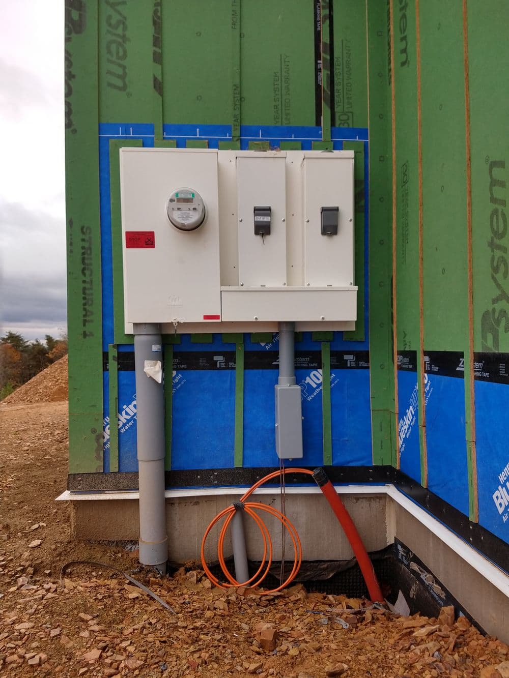 Electrical meter and utility panel on a building under construction with green wrap.